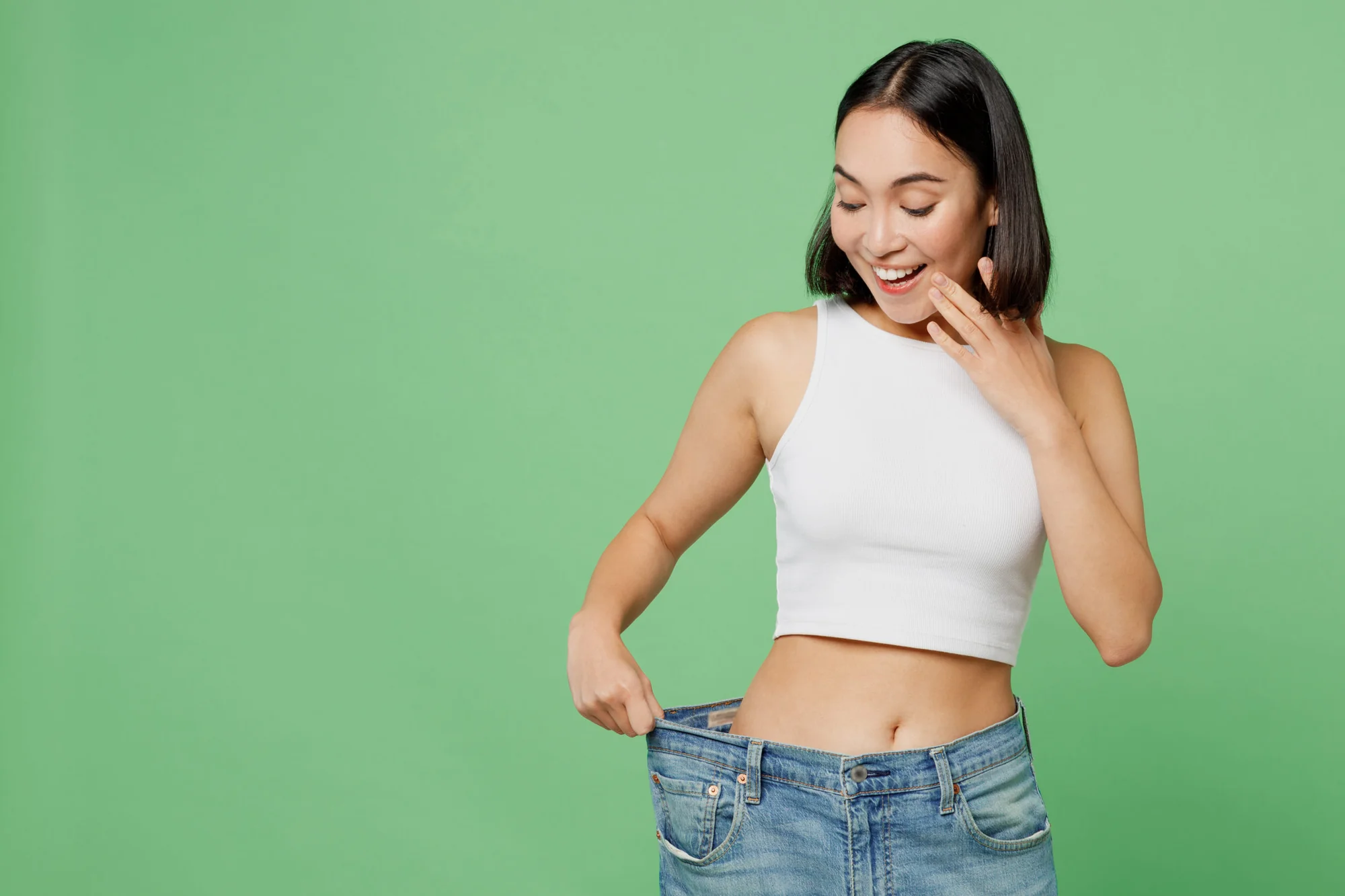 Young happy woman wears white clothes and show loose pants on waist after weight loss in Salt Lake City, UT | Santosh Yoga Institute
